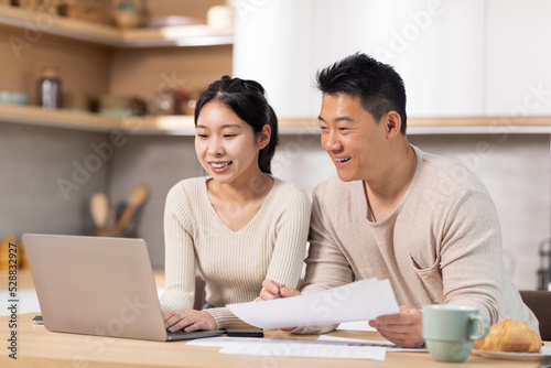 Cheerful asian couple paying bills on Internet, using laptop