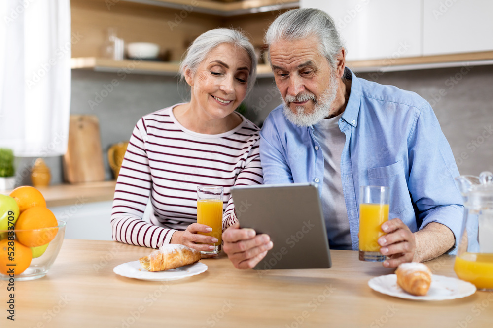 Married Elderly Couple Using Digital Tablet While Having Breakfast In Kitchen Together Married Elderly Couple Using Digital Tablet While Having Breakfast In Kitchen Together
