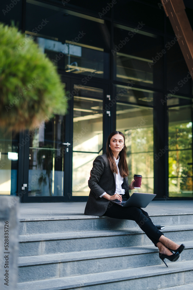 Confident business woman working online on laptop sitting on stairs front of office buildings at downtown. Business persone working remote. Outdoor. Freelancers Confident business woman working online on laptop sitting on stairs front of office buildings at downtown. Business persone working remote. Outdoor. Freelancers