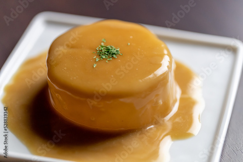 Foto 白皿に盛り付けられた、おでん大根のポルチーニソース。じっくり煮込んだ大根に、芳醇な香りのポルチーニクリームソースをたっぷりとかけ、パセリを散らした一皿。和と洋が調和した創作メニューの魅力を伝える販促素材に。 | Simmered Daikon radish with rich porcini sauce