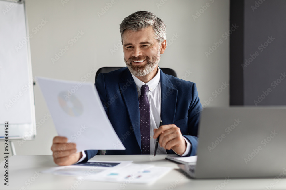 Smiling Middle Aged Businessman Working With Papers At Desk In Office