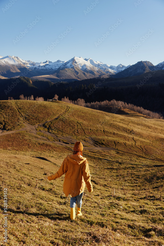 Woman's back full-length running up the hill and looking at the mountains in yellow raincoat and jeans in the autumn happy trip in the sunset sunset camping, freedom lifestyle 