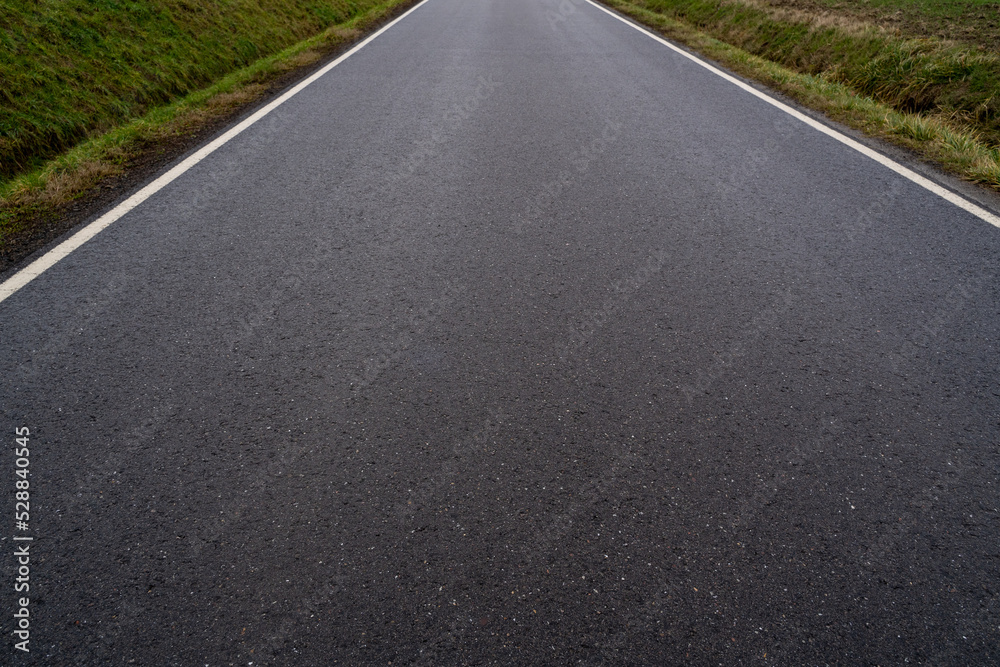 Close up of an asphalt road between grassy fields in autumn