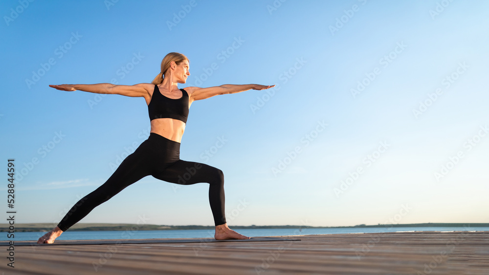 Beautiful Middle Aged Woman Practicing Yoga Outdoors, Standing In Warrior Pose Beautiful Middle Aged Woman Practicing Yoga Outdoors, Standing In Warrior Pose