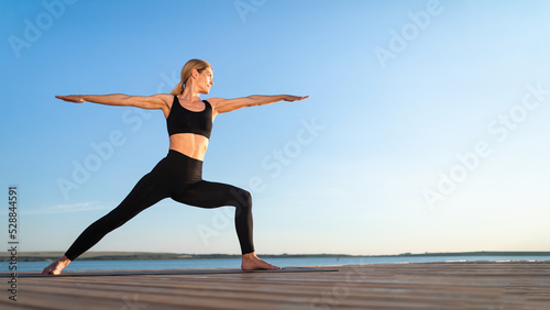 Beautiful Middle Aged Woman Practicing Yoga Outdoors  Standing In Warrior Pose