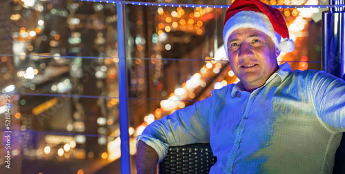 Canvas Print Happy smiling man in a santa hat against the backdrop of the lights of a big city