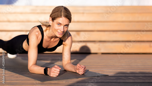 Athletic Middle Aged Female Training Outdoors, Making Plank Exercise © Prostock-studio