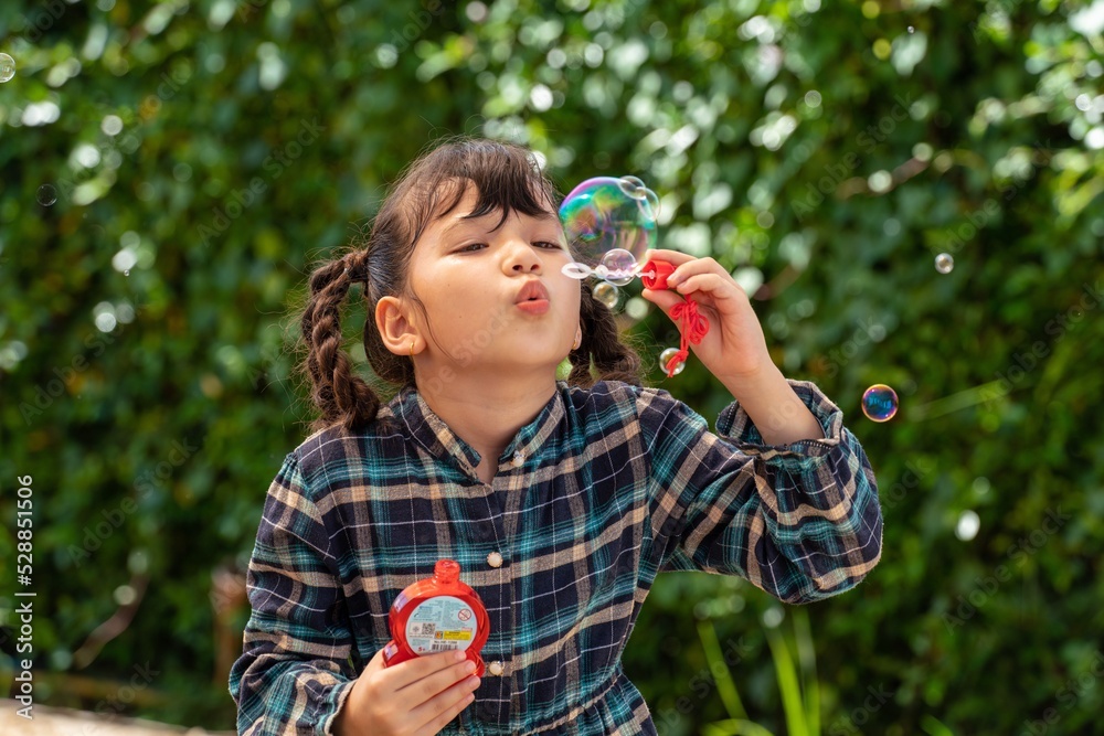 Cute asian mix caucasian female kid happily and excited while playing with bubble blowing in a garden
