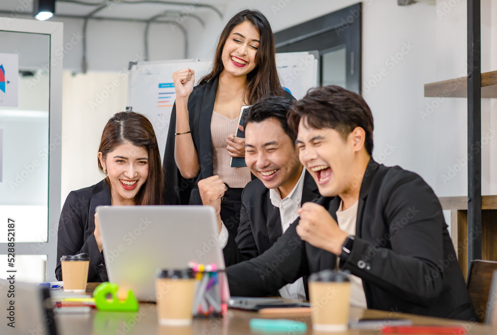 Obraz premium Group of millennial Asian young professional successful male businessmen and female businesswomen in formal suit sitting standing smiling screaming shouting holding fists up celebrating together