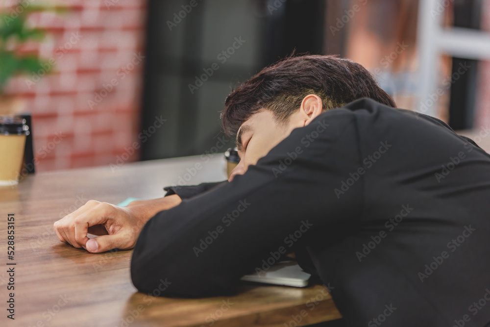 Obraz premium Asian young tired exhausted businesswoman in formal suit sitting napping on table while male female businesspeople colleagues closed eyes take break sleeping together after working late overtime