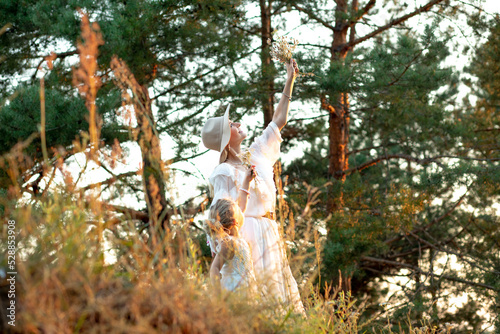 Side view of happy family standing near pines in park forest in summer. Young woman raising bouquet high, having fun. photo