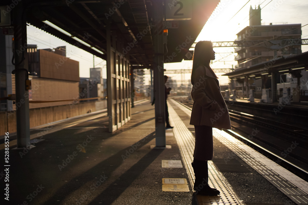 Silhouette of an Asian ladies with autumn wear standing at the railway station with sunset