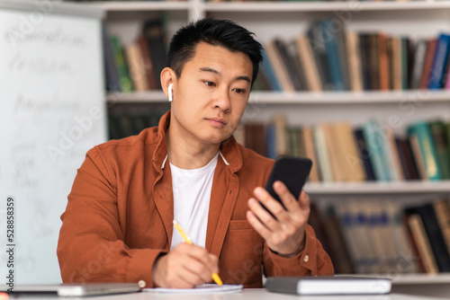 Asian Middle Aged Man Using Smartphone Learning Online In Library