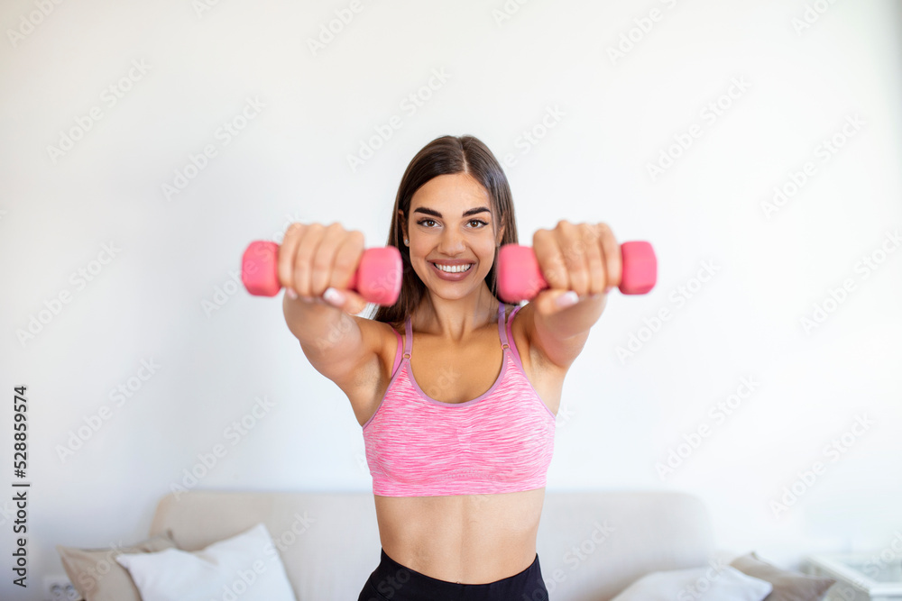 Woman exercising with dumbbells at home. Sporty beautiful woman exercising at home to stay fit. Young woman exercising at home in a living room. Fitness, workout, healthy living and diet concept. Woman exercising with dumbbells at home. Sporty beautiful woman exercising at home to stay fit. Young woman exercising at home in a living room. Fitness, workout, healthy living and diet concept.