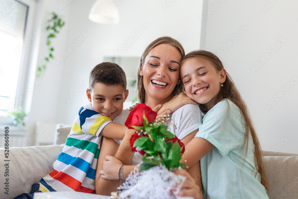 Happy children giving gift an flowers to mother. Happy Mothers Day! Children boy and girl congratulate smiling mother, give her flowers bouquet of roses and a gift box during holiday celebration Happy children giving gift an flowers to mother. Happy Mothers Day! Children boy and girl congratulate smiling mother, give her flowers bouquet of roses and a gift box during holiday celebration