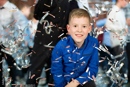 Happy little boy in confetti.Magic time - Portrait of a very happy child with hands smiling while falling confetti. At a children's party.