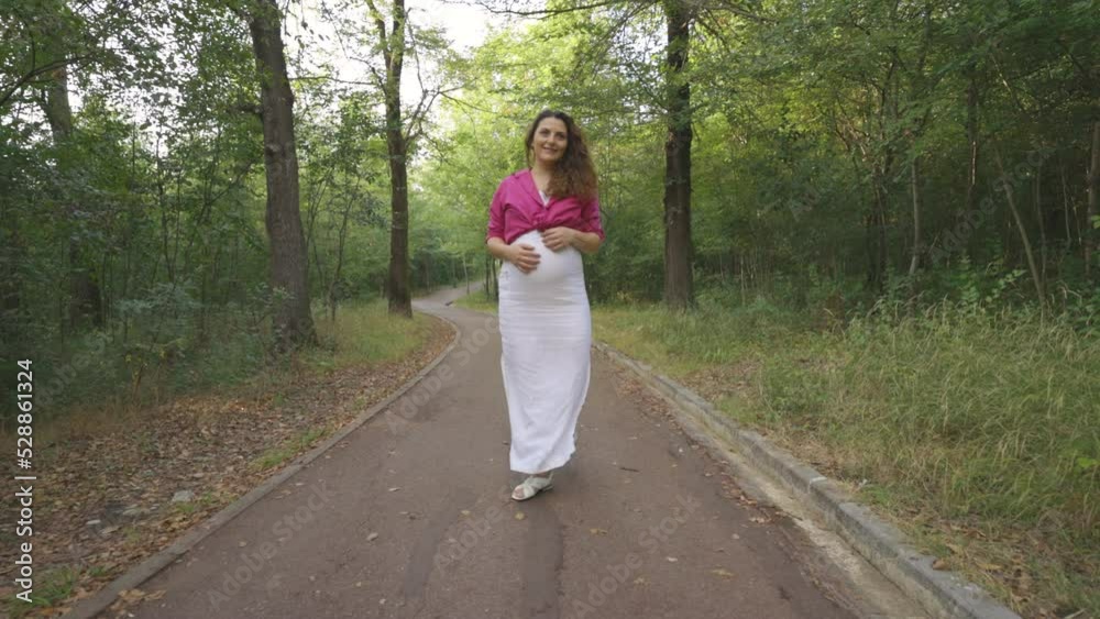Happy Pregnant Woman Expectant Mother Walking Alone in Nature, Attractive Curly Casually Dressed Mom Turning Around Stroking Caressing Touching Her Belly Smiling, Childbearing Love, followed by camera Happy Pregnant Woman Expectant Mother Walking Alone in Nature, Attractive Curly Casually Dressed Mom Turning Around Stroking Caressing Touching Her Belly Smiling, Childbearing Love, followed by camera