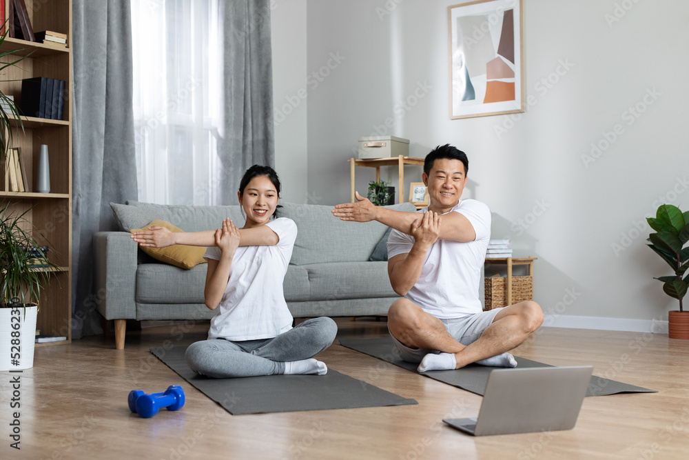 Happy korean family having morning yoga at home, using notebook Happy korean family having morning yoga at home, using notebook