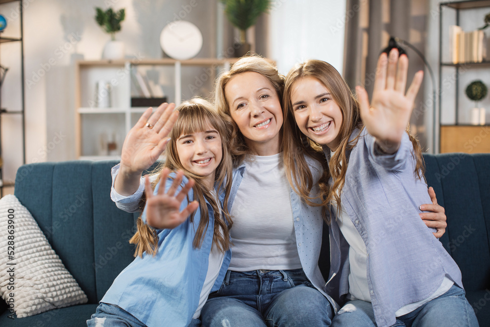 Happy mom and two little sibling kids enjoying leisure at home together, relaxing on couch, hugging, waving their hands. Loving mother embracing sweet children with care, affection. Family concept. Happy mom and two little sibling kids enjoying leisure at home together, relaxing on couch, hugging, waving their hands. Loving mother embracing sweet children with care, affection. Family concept.