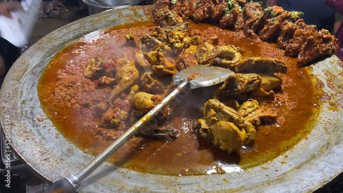 In the shop of Kolkata, a vendor is cooking or braising chicken over a high flame in a big Tawa photo