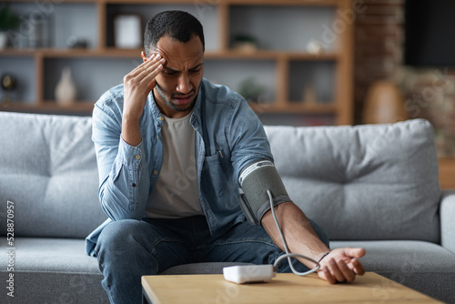 Sick Young Black Man Checking Blood Pressure With Modern Tonometer At Home photo