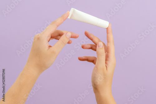Hand holds plastic cream battle isolated on lilac background. Beauty concept. Packaging tube for cosmetic products