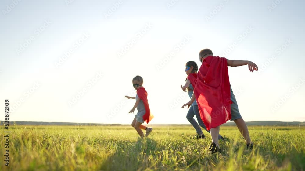 Happy family. Children dressed as superheroes play in the park. Superhero teamwork. Strong children dream of victory. Children are superheroes winners. Family game in nature. Superheroes in red capes Happy family. Children dressed as superheroes play in the park. Superhero teamwork. Strong children dream of victory. Children are superheroes winners. Family game in nature. Superheroes in red capes
