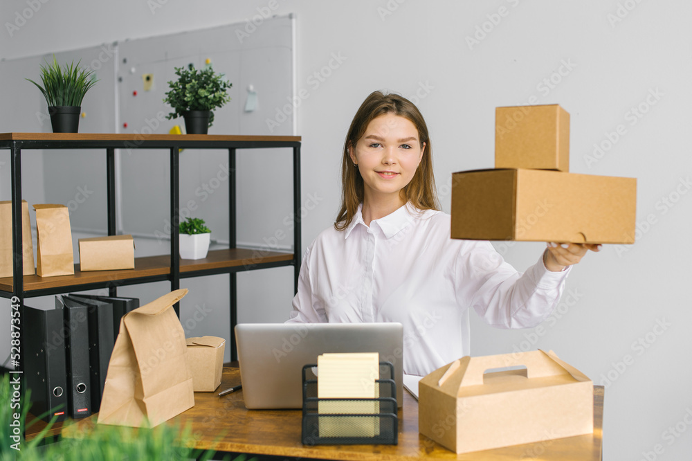 A cute girl in a white shirt is sitting in the office and holding eco food packaging in her hands and smiling