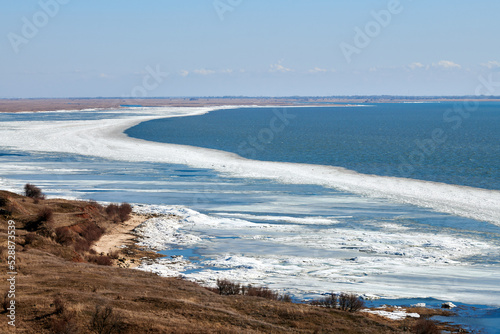 Wall Mural February seashore with melting ice near shore, seasonally nature landscape of co