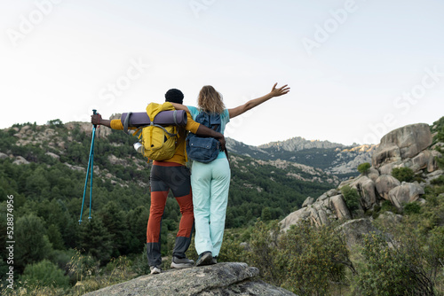 Multiracial couple trekking on top of the mountain, back view, traveling backpackers, digital nomads.