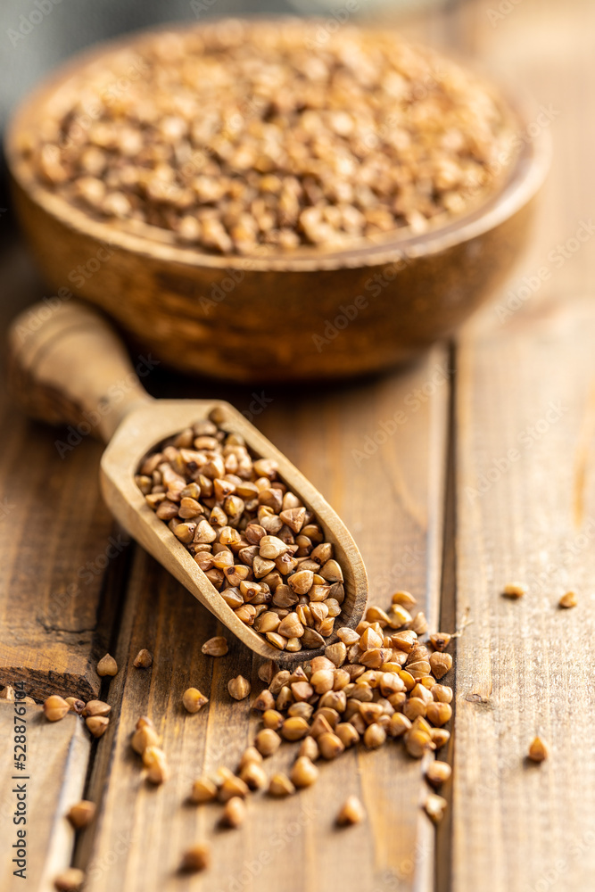 Uncooked buckwheat grain in wooden scoop on wooden table. Uncooked buckwheat grain in wooden scoop on wooden table.