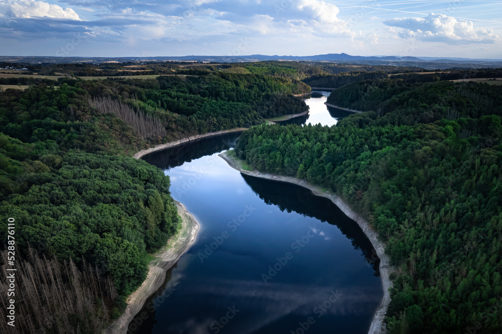 Aerial view of a blue river in a dam and a lush green forest, mountains in the background, in Germany, Europe
