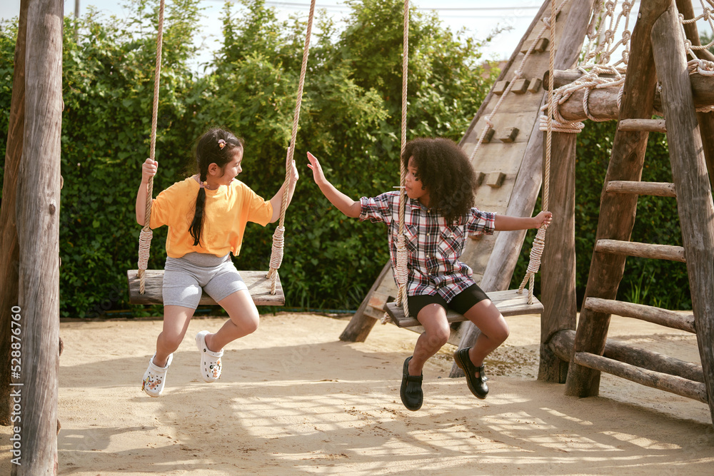 Two kids girl are playing on the swing in the outdoor playground.