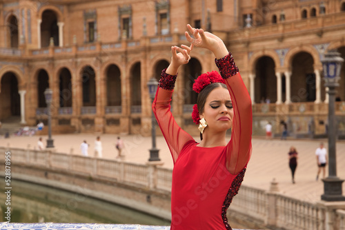 Young teenage woman in red dance suit with red carnations in her hair doing flamenco dance poses. Flamenco concept, dance, art, typical Spanish dance.
