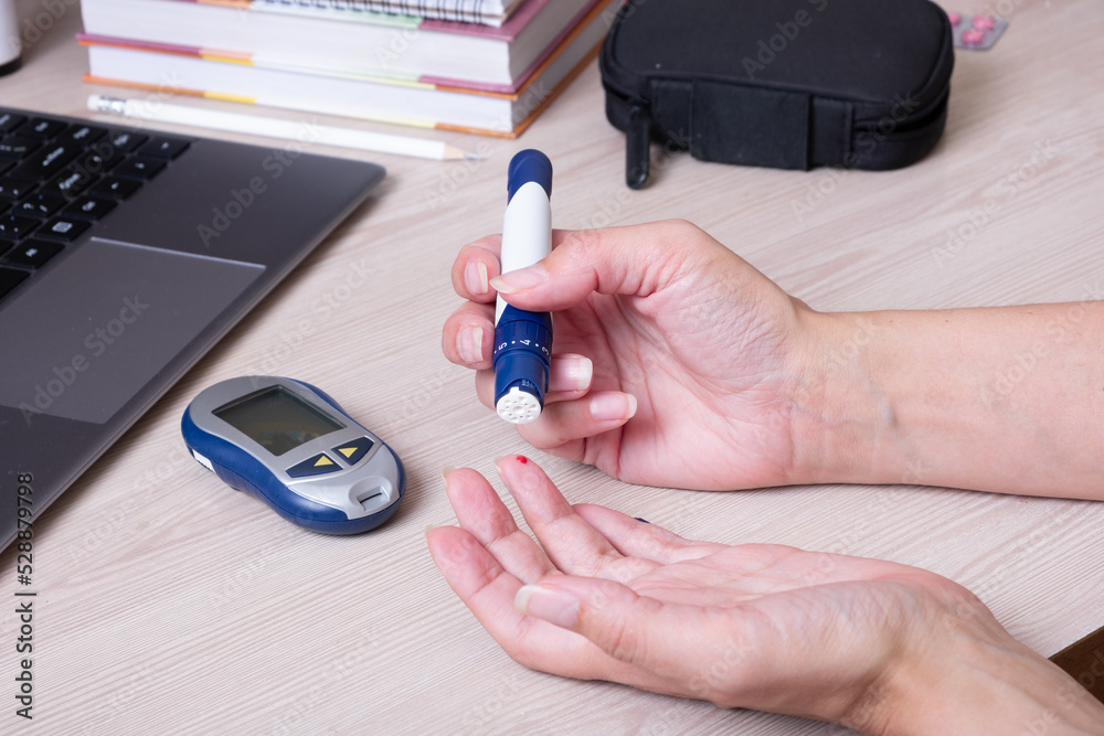 Female hands with a glucometer at the desk. The lifestyle of a person with diabetes, measuring the level of glucose