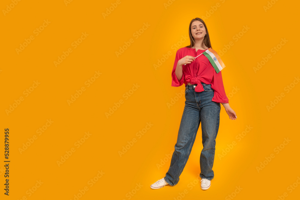 Full-length portrait of European teenage girl in youth clothes with the flag of India in her hands. Copy space. Full-length portrait of European teenage girl in youth clothes with the flag of India in her hands. Copy space.