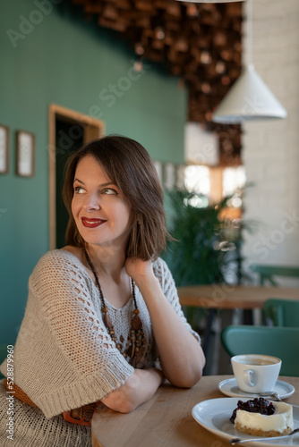 Portrait of young woman at table in cafe. Girl ordered coffee and dessert in confectionery. Vertical frame.