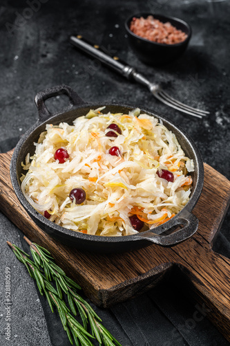 Sauerkraut in a skillet with black pepper and cranberry, Fermented cabbage. Black background. Top view