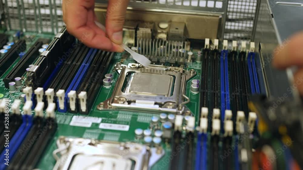 A male technical engineer in a server hardware assembly room applies thermal paste to a processor close-up A male technical engineer in a server hardware assembly room applies thermal paste to a processor close-up