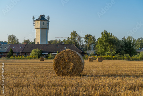 Hay bales (hay balls, haycock or haystack) on a farm field. Straw bales on agriculture field. Rural farm land nature, Countryside landscape after harvest. With train railway station in background. photo
