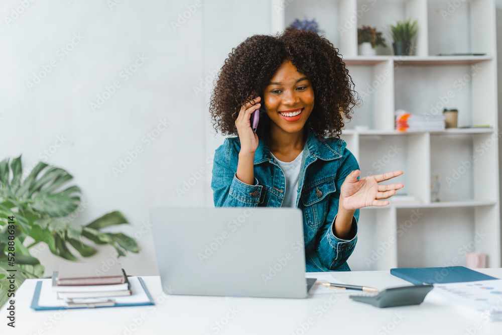 Young female freelancer talking on phone and using laptop at desk. Young female freelancer talking on phone and using laptop at desk.