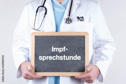 Arzt mit einer Tafel auf der Impfsprechstunde steht