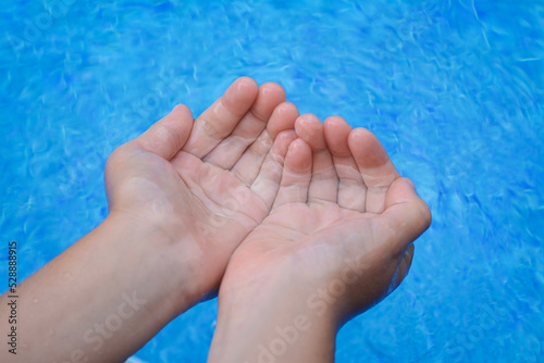 Girl holding water in hands above pool, closeup
