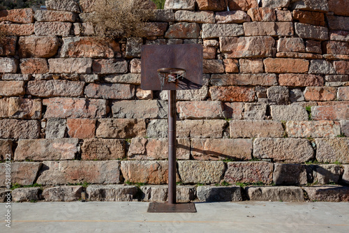 Old basketball hoop centered in frame with stone wall in the background photo