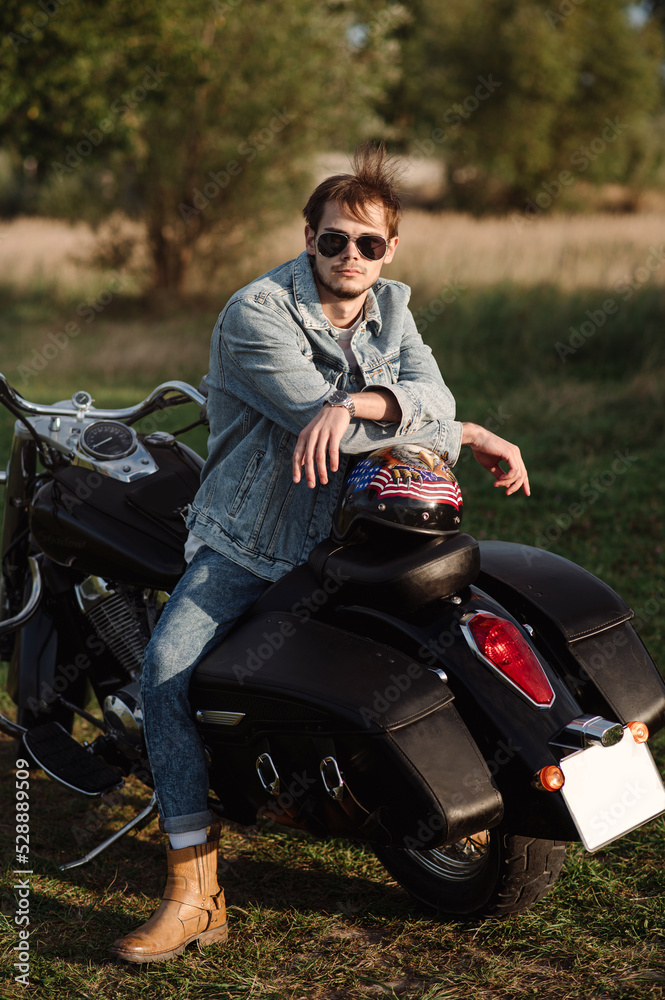 Handsome male biker wearing a jeans clothes is sitting on the motor bike
