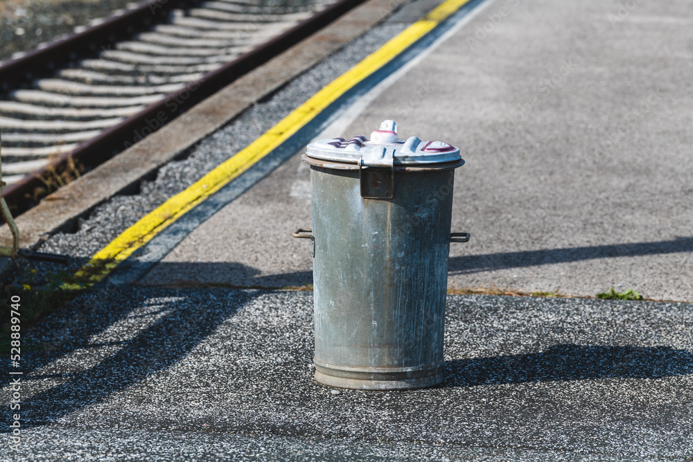 Mülltonne wartet auf den Zug - Mülltonne aus Metall steht neben einem Gleis in einem Güterbahnhof Mülltonne wartet auf den Zug - Mülltonne aus Metall steht neben einem Gleis in einem Güterbahnhof