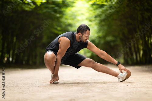 Active black guy stretching in public park