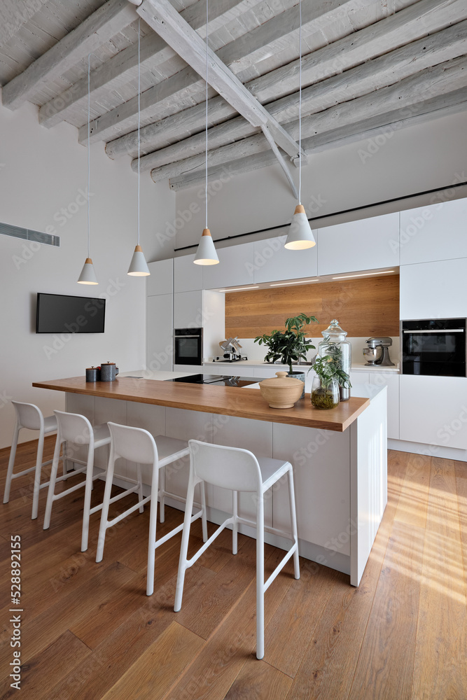 interior view of a modern white kitchen, in the foreground the island kitchen with stools, the lighting is entrusted to four pendant lamps, the floor and ceiling are made of wood