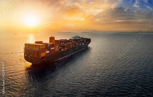 Aerial view of a large, heavy loaded container cargo ship sailing over calm sea into the sunset