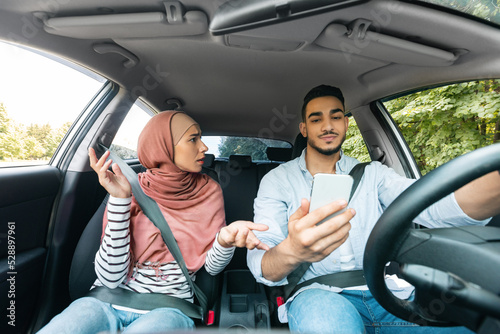 Disappointed millennial muslim woman in hijab swears at her husband with smartphone while traveling together © Prostock-studio